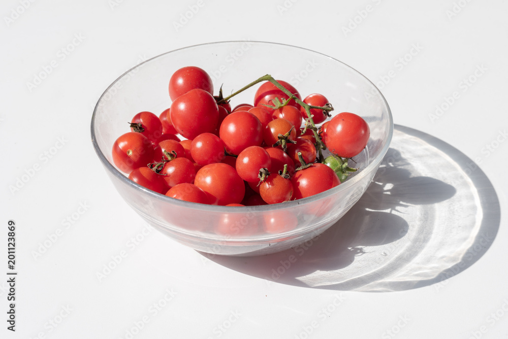 Homegrown red cherry tomatoes in glass bowl on white table with hard shadow from bright sunlight (selective focus) Homegrown red cherry tomatoes in glass bowl on white table with hard shadow from bright sunlight (selective focus)