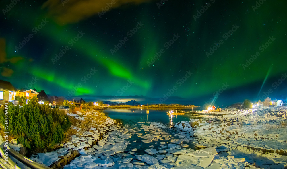 Amazing outdoor view of green aurora borealis in the sky during night and small and medium pieces of Ice left behind during a low tide on a frozen lake