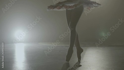Graceful sensual ballerina wearing white outfit dancing and spinning elegantly in a dark background with spotlight
