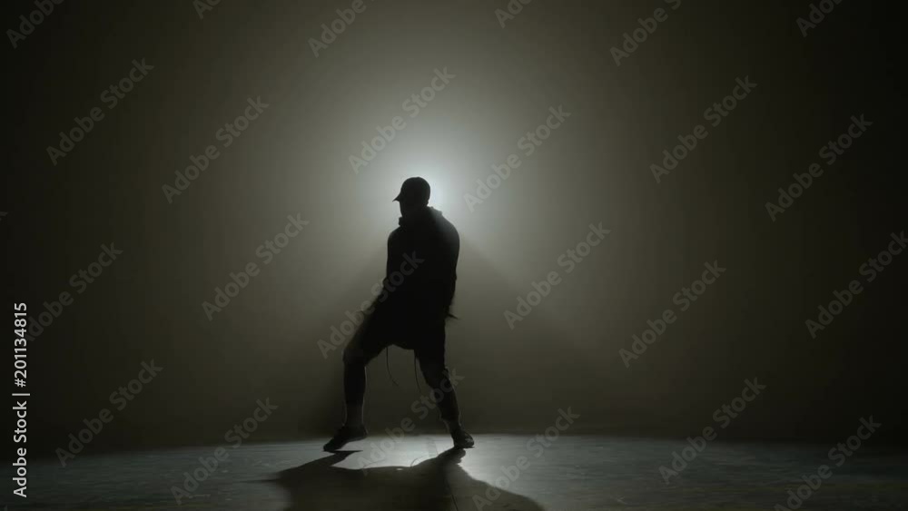 Silhouette of a talented young dancer dancing hip hop street dance on a stage in front of the spotlight Silhouette of a talented young dancer dancing hip hop street dance on a stage in front of the spotlight