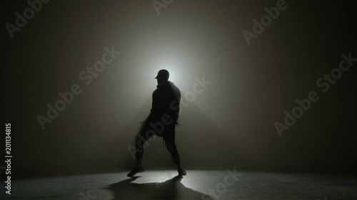 Silhouette of a talented young dancer dancing hip hop street dance on a stage in front of the spotlight