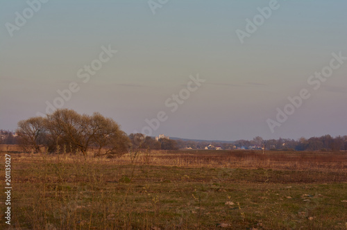 Early spring in nature. Sunset on a rural landscape. View of the city. Outdoor recreation.Stock image for design. Trees and grass on a meadow