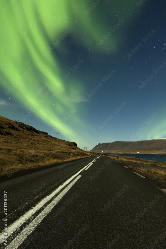Northern lights / Aurora Borealis glowing above night road in beautiful Iceland landscape