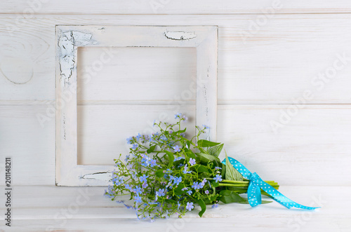 Forget-me-not flowers bouquet and vintage photo frame on white wooden shabby board