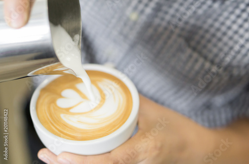 Woman barista pouring stream milk for making latte art coffee with tulip shape in white cup, selective and soft focus