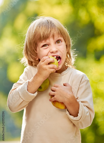 Portrait of cute little blonde boy with milk teeth eating apple