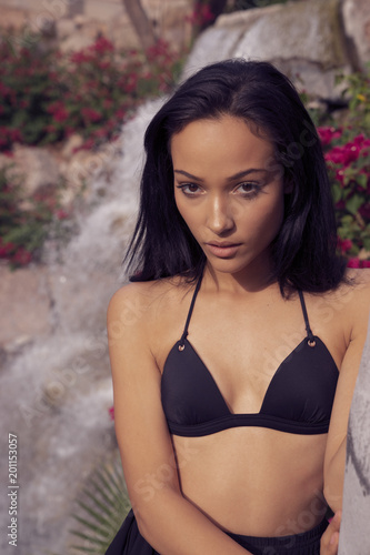 Beautiful young woman wearing bikini surrounded by blooming flowers.