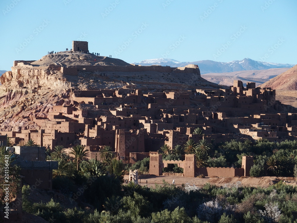 Scenery of Kasbah Ait Ben Haddou, green exotic palm trees at oasis on african Atlas Mountains range landscape, Morocco