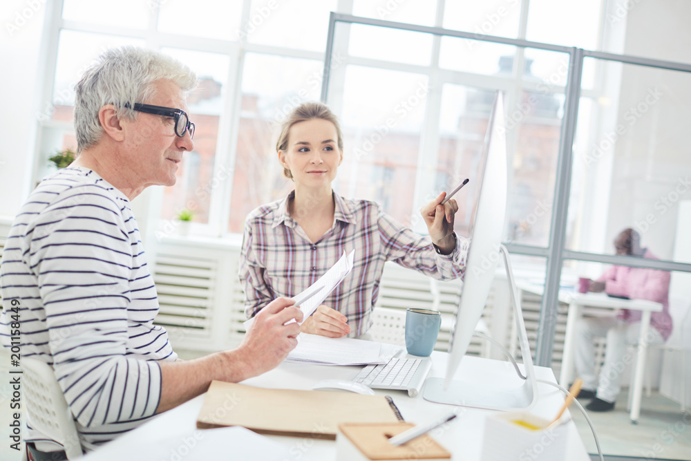 Businesswoman pointing at computer screen and discussing presentation with her coworker Businesswoman pointing at computer screen and discussing presentation with her coworker