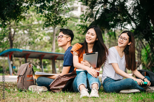A group of young or teen Asian student in university smiling and reading the book and look at the tablet or laptop computer in summer holiday.