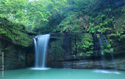 A cool refreshing waterfall tumbling down the cliff into an emerald pond hidden in a mysterious forest of lush greenery   Scenic view of a beautiful waterfall and intriguing river potholes in Taiwan