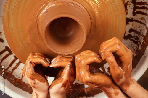 hands of a man and a woman in the shape of a heart in clay on a potter's wheel mold a vase. The potter works in a pottery workshop with clay. the concept of Valentine's Day and love in pottery