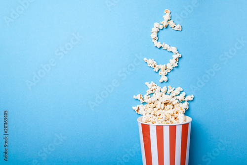 Concept ticket prices or ticket office movie. Spilled popcorn in the form of a dollar sign from a paper bucket in a red strip on a blue background. Copy space for text photo
