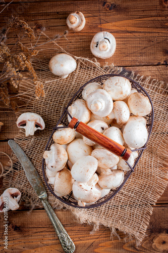 Raw fresh mushrooms in a metal basket on a wooden table, top view