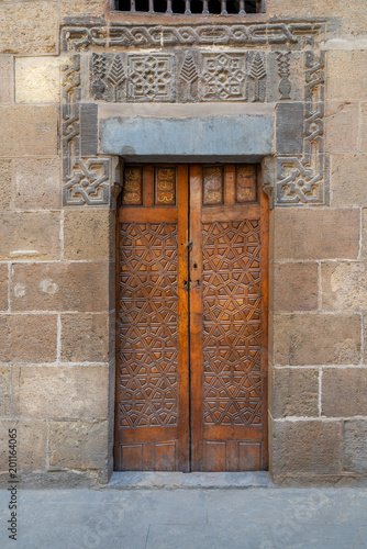 Wooden ornate door with geometrical engraved patterns on external old decorated bricks stone wall leading to Beit (house) Al Sehemy historical house, Cairo, Egypt photo