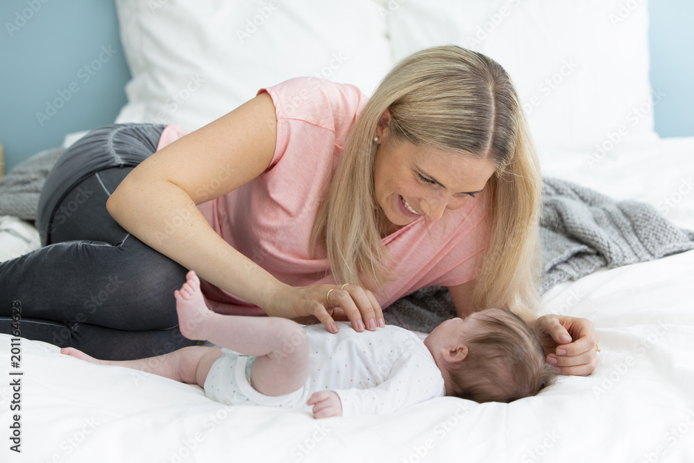 young, beautiful and blond mother with pink shirt is cuddling with her baby in bed young, beautiful and blond mother with pink shirt is cuddling with her baby in bed