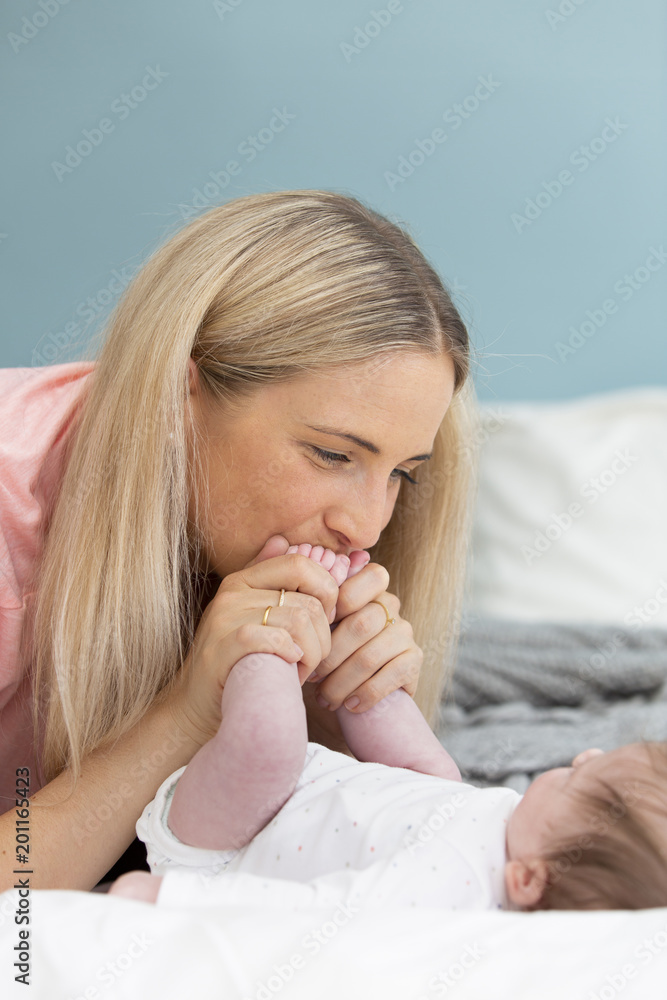 young, beautiful and blond mother with pink shirt is cuddling with her baby in bed young, beautiful and blond mother with pink shirt is cuddling with her baby in bed