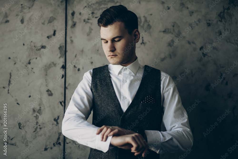 Portrait of young businessman looking at his smartwatch against a grey wall.