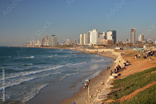 Widok na zatokę Morza Śródziemnego, plażę, nabrzeże ze spacerującymi i odpoczywającymi ludźmi, w tle wysokie nowoczesne budynki, Tel Awiw, Izrael, fale na morzu, błękitne niebo © Wioletta