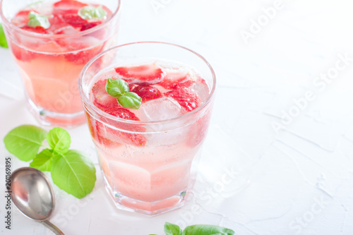 Fresh cool summer drink with strawberries and green basil in glass glasses on white table, horizontal, copy space