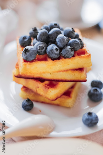 Belgian waffles with blueberries on the light wooden table. Healthy breakfast. 