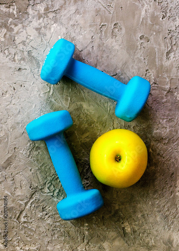 Turquoise dumbbells with measuring tape and yellow apple on concrete background. Free space for your text. Sport concept