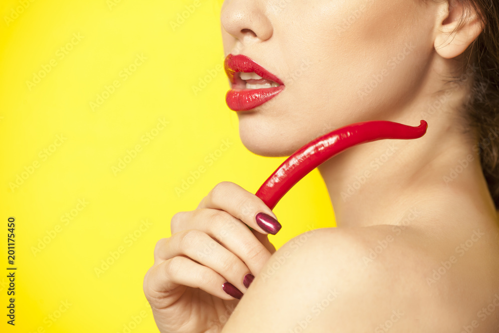 Young sexy woman holding a red chili with her fingers on yellow background Young sexy woman holding a red chili with her fingers on yellow background