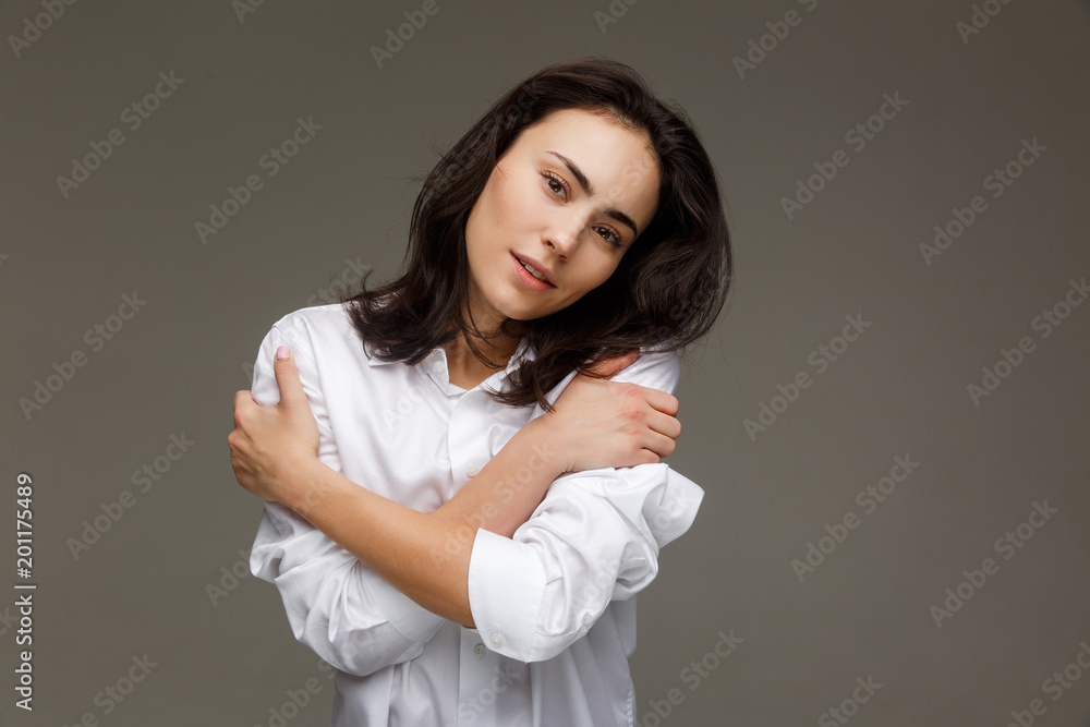 Beautiful girl in a white shirt embraces herself. On a light background. Beautiful girl in a white shirt embraces herself. On a light background.