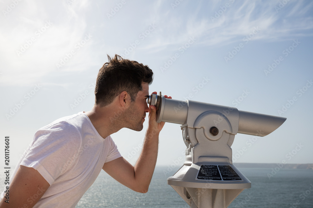 Man looking through binoculars at ocean