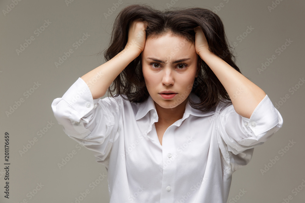 Beautiful girl in a white shirt shows emotions - headache. On a light background. Beautiful girl in a white shirt shows emotions - headache. On a light background.