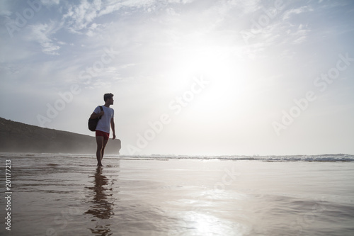 Young man strolling alone on beach in swimming trunks