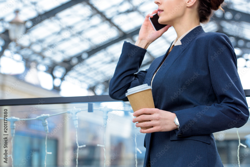 cropped image of businesswoman talking by smartphone and holding coffee in paper cup cropped image of businesswoman talking by smartphone and holding coffee in paper cup