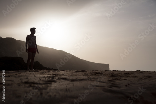 Profile of man at the beach in front of cliff during sunset photo