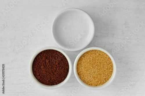 Homemade face scrub made out of coconut oil, coffee powder and brown sugar on wooden background