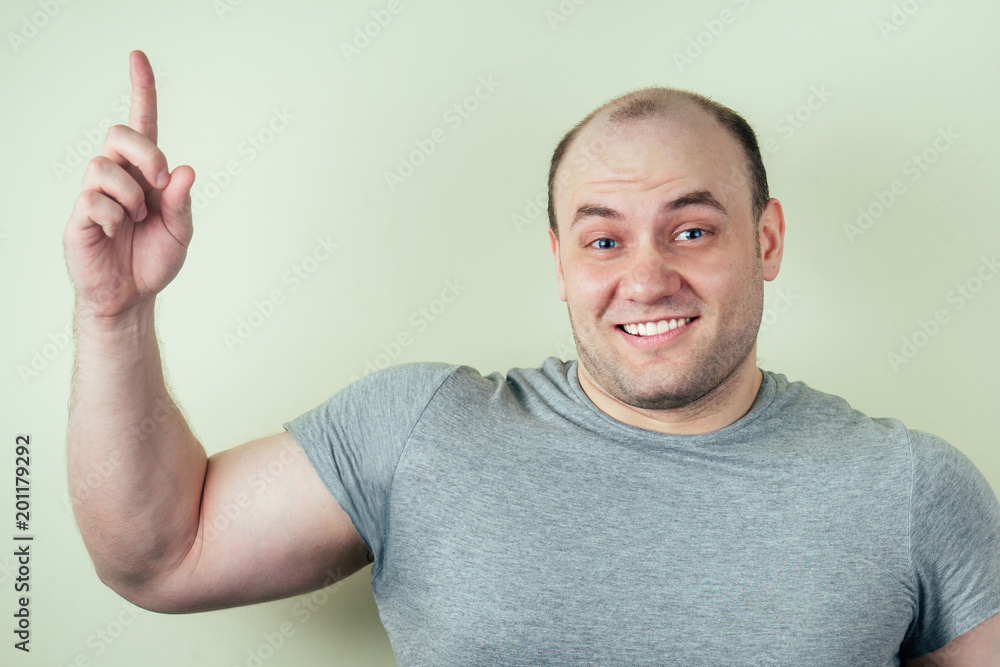 portrait of a bald man with a raised finger against a gray background. a man came up with the idea portrait of a bald man with a raised finger against a gray background. a man came up with the idea