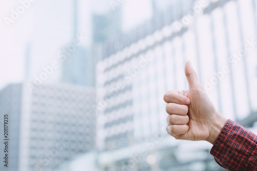 Closeup of Businessman hand showing thumb up sign against outdoor of office building background. copy leave space for text.