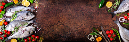 Photography Fresh uncooked fish, dorado, sea bream with lemon, herbs, vegetables and spices on rustic background