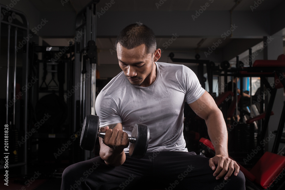Muscular builder man training his body with dumbbell in Modern fitness center Muscular builder man training his body with dumbbell in Modern fitness center