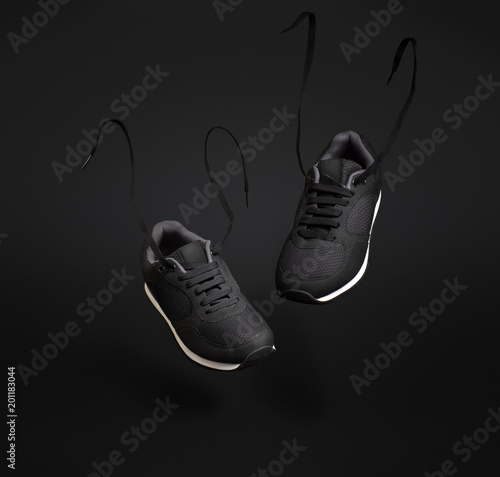 A pair of black unbranded sneakers floating in front of dark background.