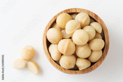 Macadamia nuts in wooden bowl on white background top view