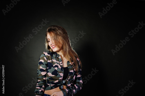 Handsome brunette girl wear military shirt and jeans, posing at studio against gray background. Studio model portrait.