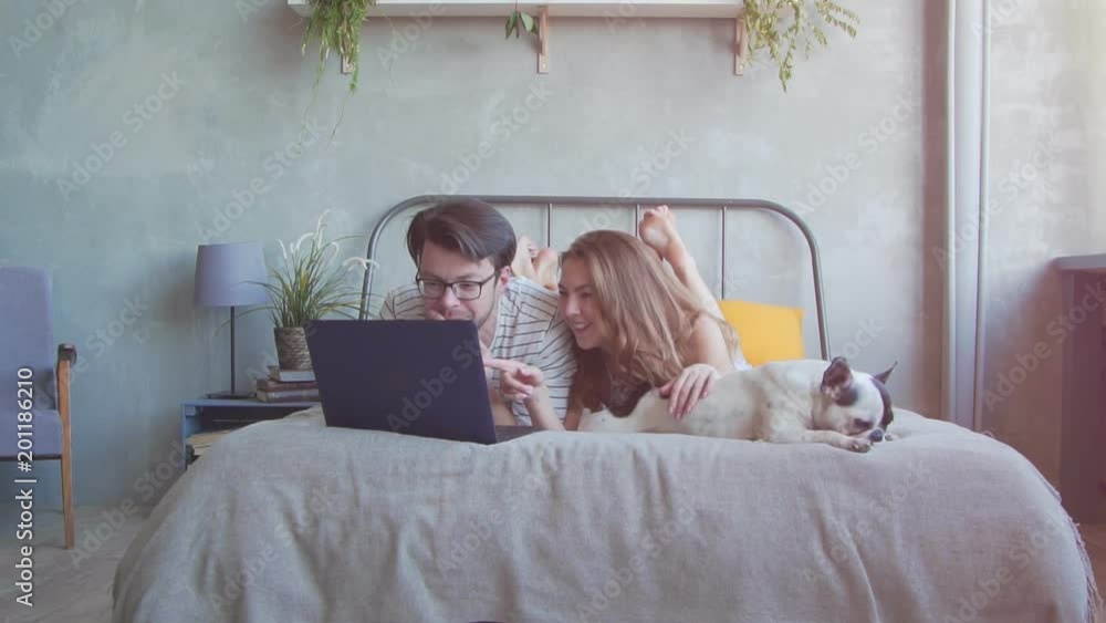 Happy young couple with french dog with laptop at home. Slow motion