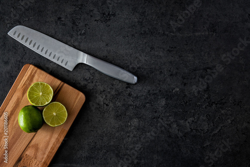 Flat lay of fresh limes on cutting board with knife on black concrete background. Horizontal top view with copy space. photo