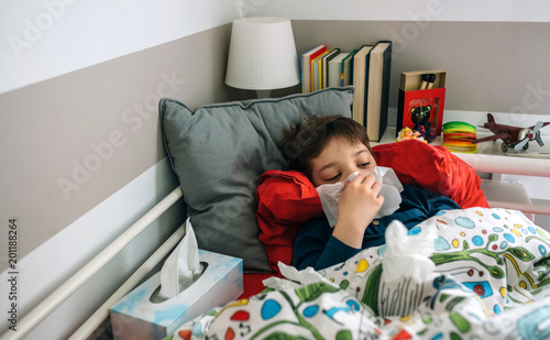Cold child lying on the bed blowing his nose with handkerchiefs