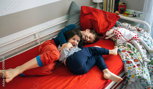 Billede på lærred Brother and sister tickling and laughing while lying on the bed