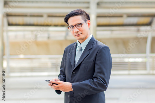 Young Asia handsome businessman with his smartphone standing on walkway of modern city.