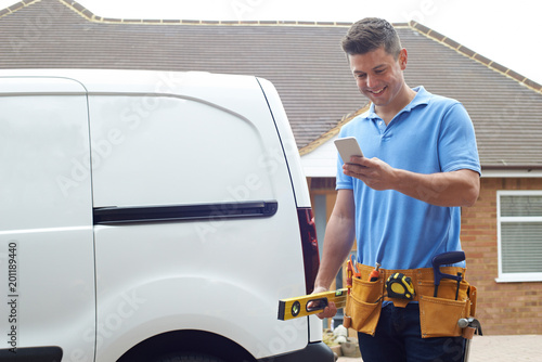 Photos Builder With Van Checking Text Messages On Mobile Phone Outside House