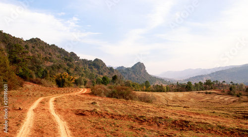 Dirt road winds between arid farmland and low mountain range in Shan State, Myanmar