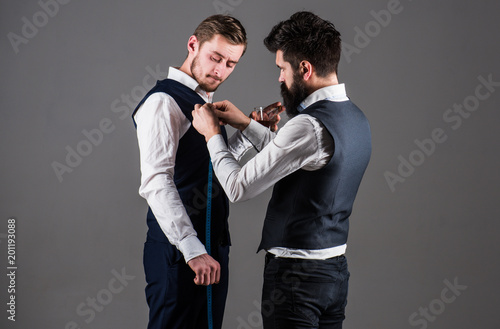 Tailor taking measurements for sewing, grey background.