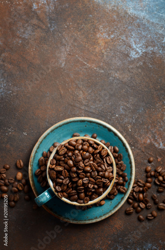 Natural organic roasted coffee beans in blue cup on dark rusty background, top view, flat lay, copy space.